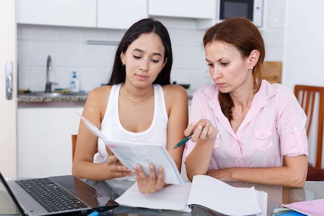 Mother and daughter looking at test booklet at the kitchen table.