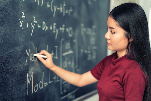 Asian student doing math problem on chalkboard