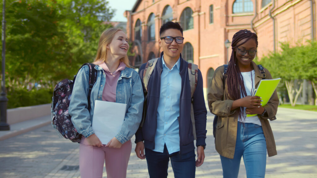 Three smiling college students walking across campus